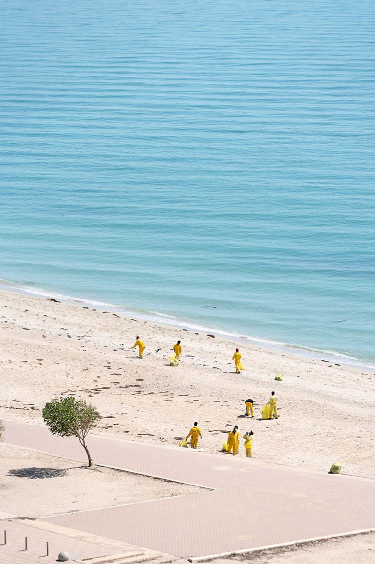 Aidan Brooks is shooting the largely empty beach from his window in Salmiya, Kuwait; this images sees workers dressed in yellow overalls cleaning seaweed after a few days of bas weather