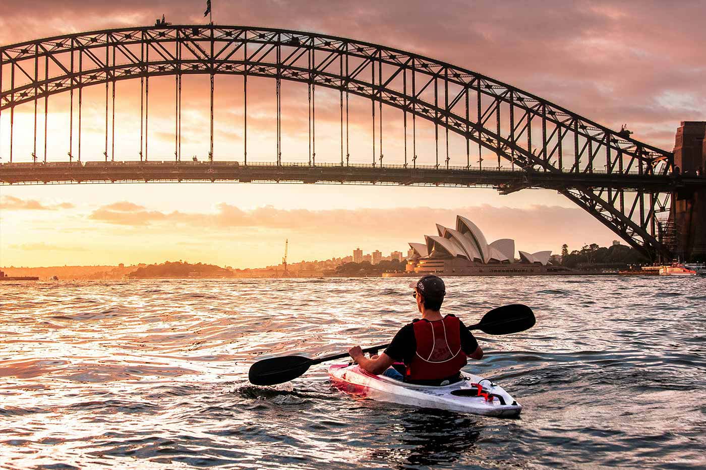 A person kayaking on Sydney Harbour with the Harbour Bridge and Opera House in the background